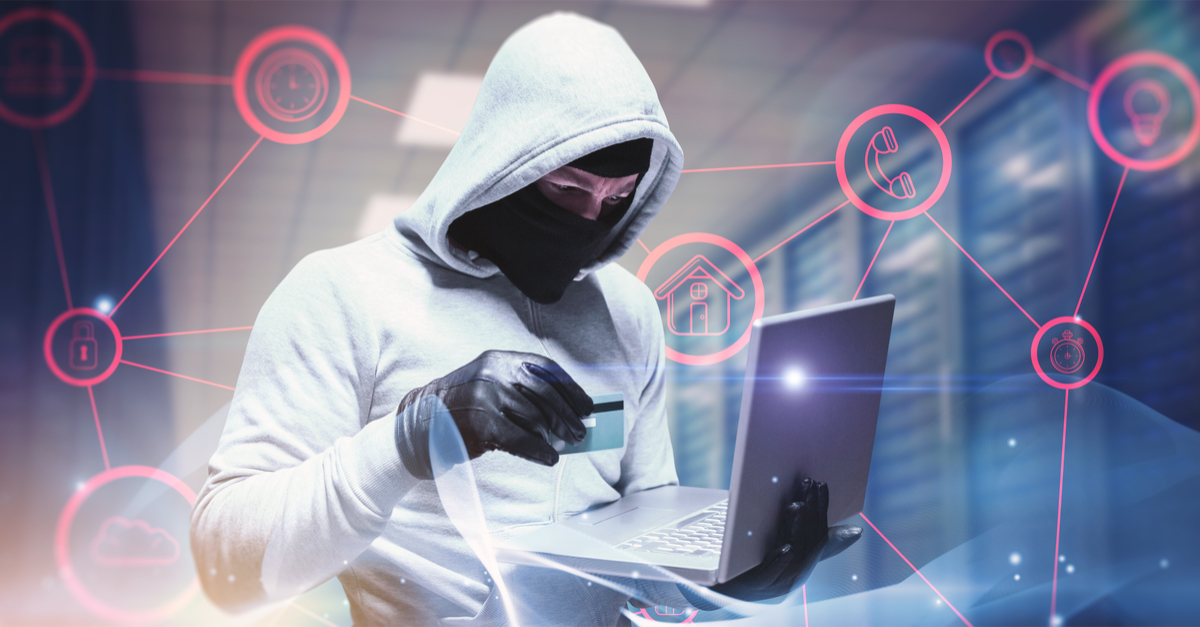 A hacker depicted as a person in a grey hoody, gloves and mask stading with a laptop in the server room. The hacker is also holding a credit or debit card.